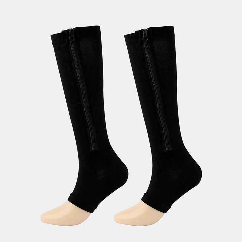 Ein Paar Tieberg™️ ZipperSocks - Kompressionsstrümpfe mit Reißverschluss in schwarz, kniehoch an Schaufensterpuppenfüßen vor einem schlichten hellen Hintergrund.