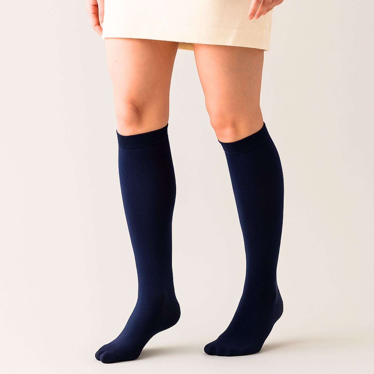 Eine Person modelliert Tieberg™️ Vitalsocks - Spürbarer Tragekomfort in dark navy, gepaart mit einem cremefarbenen Rock, vor einem schlichten hellen Hintergrund. Nur die Beine und der Unterrock sind sichtbar.