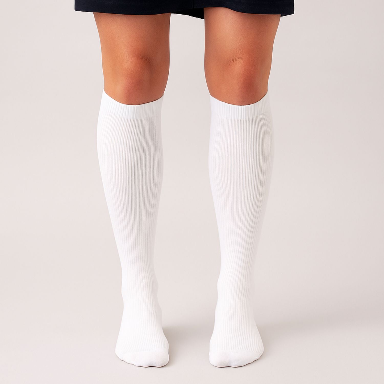 Eine Person steht mit zusammengelegten Füßen vor einem hellen Hintergrund und zeigt nur ihre Beine, die mit knielangen weißen Vitalsocks - Spürbarer Tragekomfort von Tieberg™️ bekleidet sind.