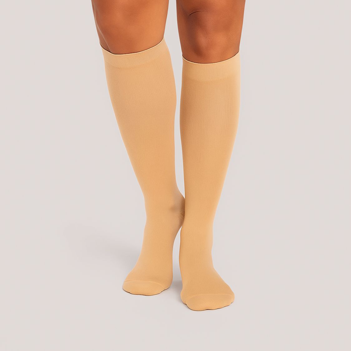 Eine Person, die Tieberg™️ Vitalsocks - Spürbarer Tragekomfort beige kniehohe Kompressionssocken trägt, steht mit den Füßen zusammen vor einem schlichten hellen Hintergrund.